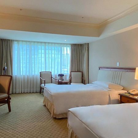 Evergreen Laurel Hotel - Taichung Esterno foto The photo shows a hotel room featuring two single beds positioned near each other. There's a light-colored carpet on the floor and a large window with sheer curtains that allows natural light to fill the space. In the room, there are two chairs place