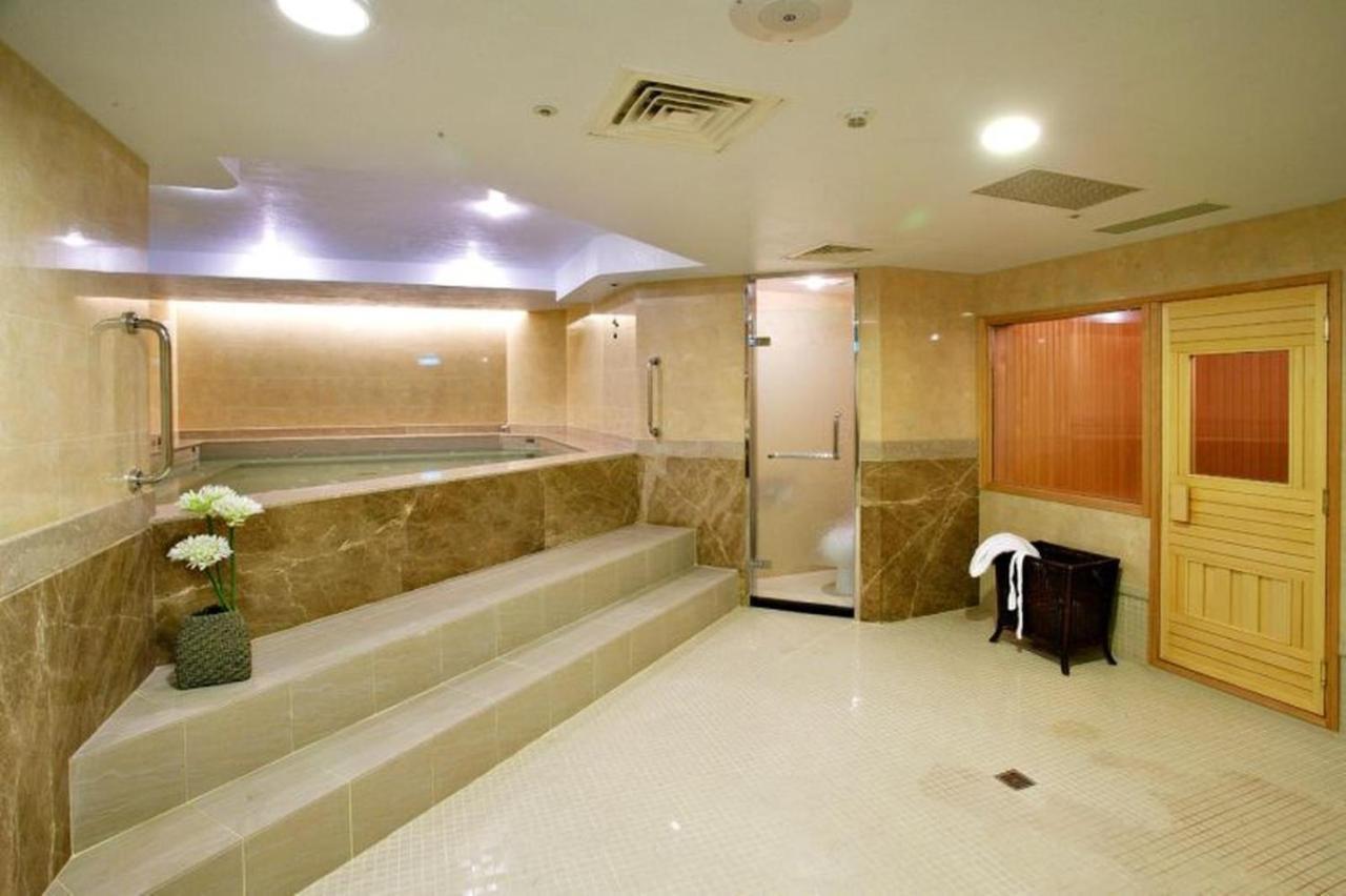 Evergreen Laurel Hotel - Taichung Esterno foto The photo shows a spacious and well-lit spa or wellness area. It features a large, recessed hot tub with steps leading up to it, surrounded by beige marble walls. There's a shower area enclosed in glass, and to the right, a wooden sauna or steam room