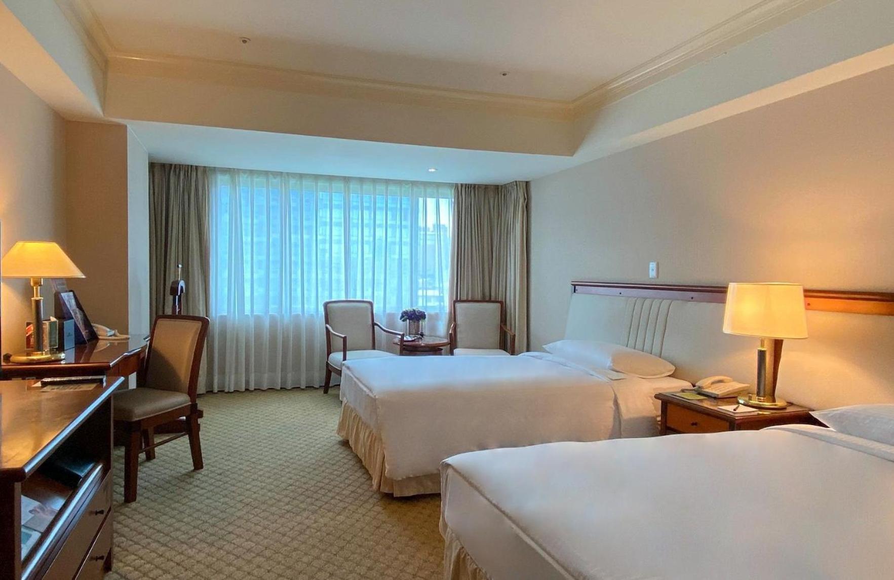 Evergreen Laurel Hotel - Taichung Esterno foto The photo shows a hotel room featuring two single beds positioned near each other. There's a light-colored carpet on the floor and a large window with sheer curtains that allows natural light to fill the space. In the room, there are two chairs place