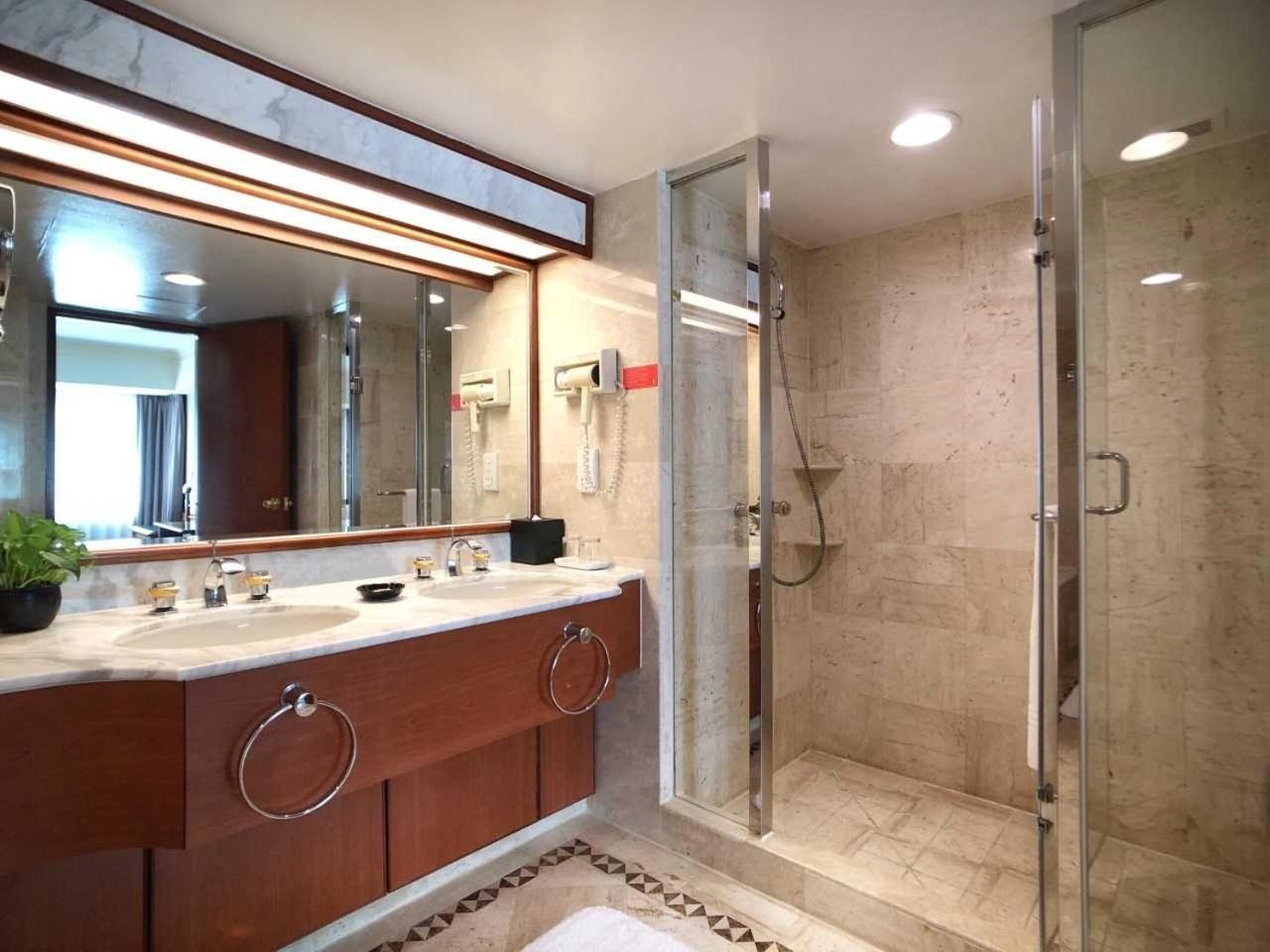 Evergreen Laurel Hotel - Taichung Esterno foto The photo depicts a modern bathroom featuring a double vanity sink with a marble countertop and wooden cabinetry. Above the sinks, there is a large mirror with integrated lighting. To one side, there is a shower enclosed in glass, showcasing a sleek 