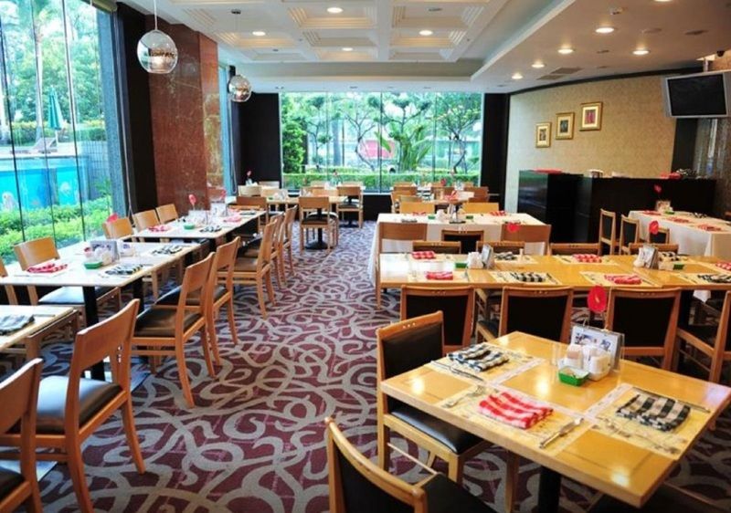 Evergreen Laurel Hotel - Taichung Esterno foto The photo shows an interior of a restaurant with a spacious layout. There are several wooden tables, each set with napkins and utensils. The floor has a decorative carpet, and large windows provide a view of greenery outside. The lighting is bright, 