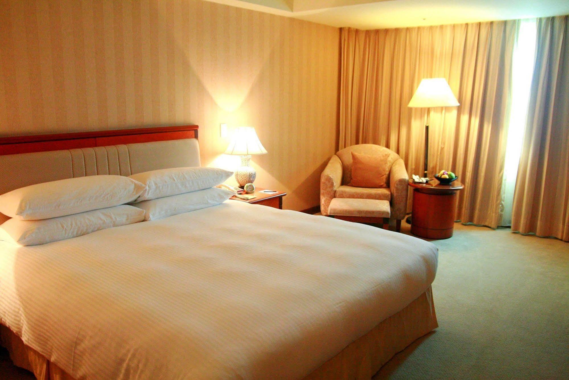 Evergreen Laurel Hotel - Taichung Esterno foto The photo shows a hotel room containing a large bed with white linens, flanked by two bedside lamps. To one side, there is a cozy armchair and a small side table with a fruit bowl or snacks. The walls are decorated in a soft, neutral color, and there