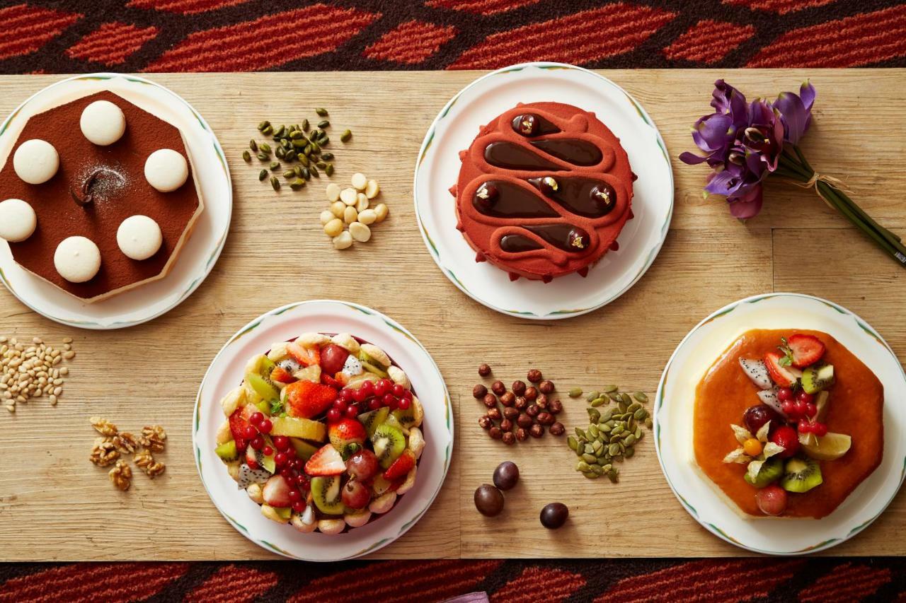 Evergreen Laurel Hotel - Taichung Esterno foto The photo displays a variety of desserts arranged on small plates. There are three main cakes or tarts:

1. **Top Left Plate**: A round chocolate cake with a smooth surface and white decorations on top.
2. **Top Middle Plate**: Another cake, possibly