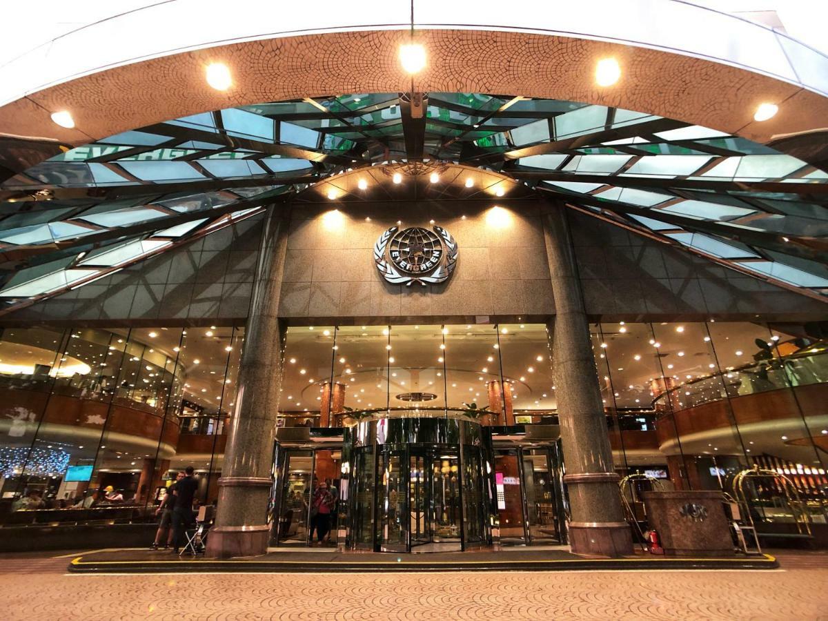 Evergreen Laurel Hotel - Taichung Esterno foto The image shows the entrance of a modern building, likely a hotel or a luxury establishment. The entrance features a large revolving door surrounded by glass panels. Above the entrance, there is a prominent logo or emblem. The overall architectural d