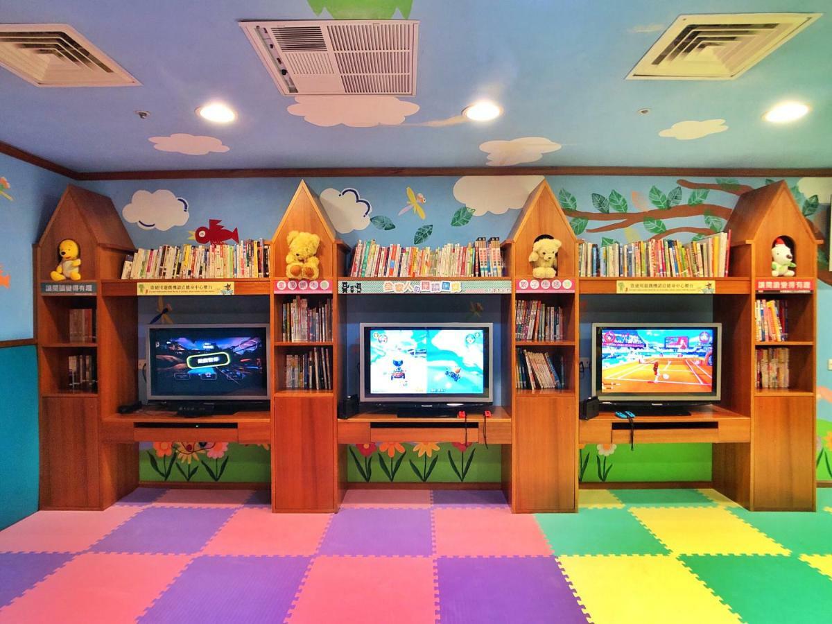 Evergreen Laurel Hotel - Taichung Esterno foto The photo shows a colorful and playful room designed for children. In the center, there are three wooden gaming stations, each equipped with a television screen and surrounded by shelves filled with books. The walls are decorated with cheerful images