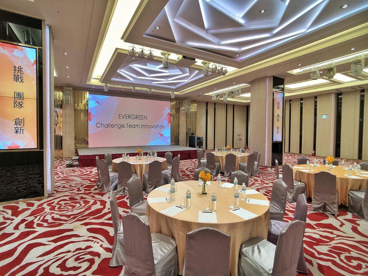 Evergreen Laurel Hotel - Taichung Esterno foto The photo shows a conference or event space set up for a gathering. The room features several round tables with light-colored tablecloths and chairs, each with decoration, possibly for dining or discussion. A large screen displays the text "EVERGREEN