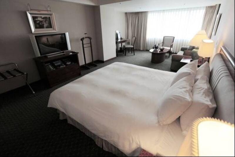 Evergreen Laurel Hotel - Taichung Esterno foto The photo shows a hotel room featuring a large bed with white bedding. There is a flat-screen television on a wooden cabinet opposite the bed. Nearby, there are two armchairs and a small table, creating a cozy seating area. Large windows allow natura
